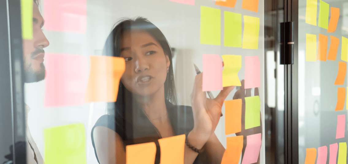 Colleagues placing sticky notes on transparent display board